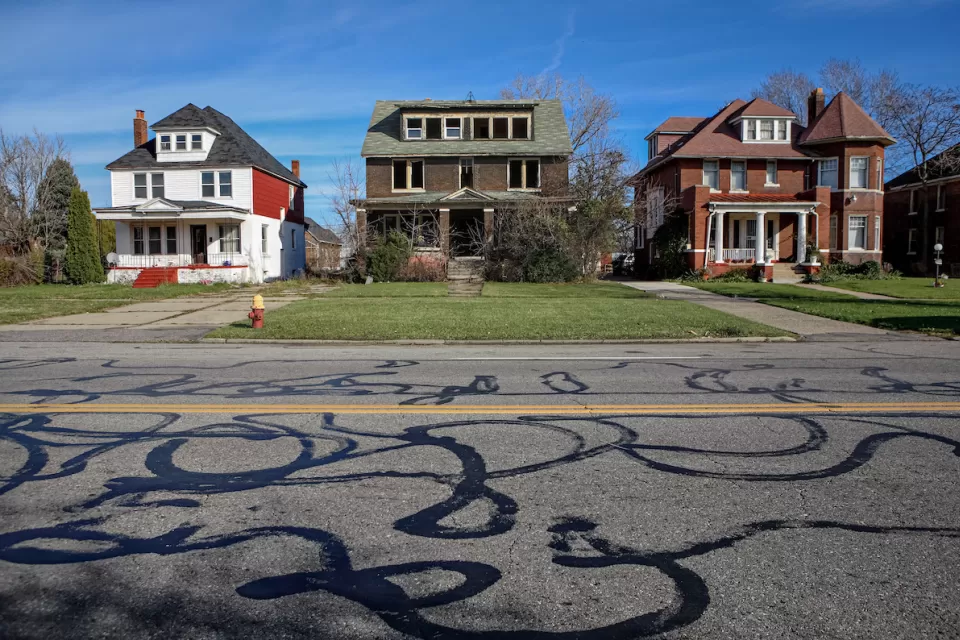 Three two-story houses on residential street in Detroit, Michigan. Center house appears abandoned.
